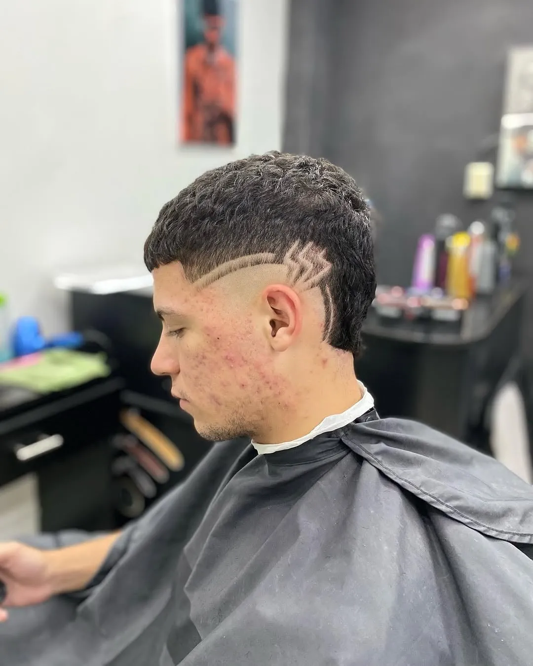 Taper fade con diseño de rayo en el costado de la cabeza y cabello corto rizado arriba