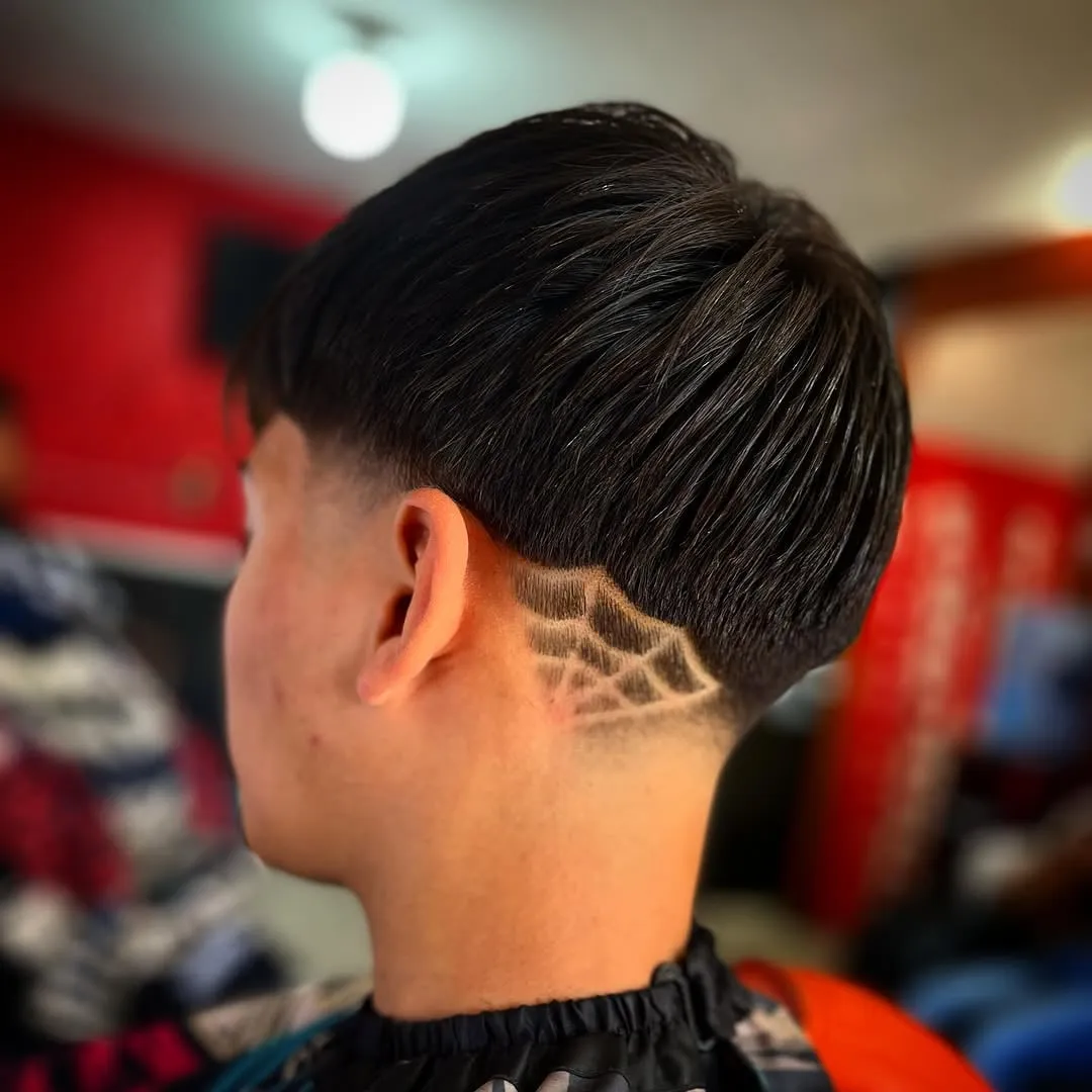 Taper fade bajo visto de lado con un diseño de telaraña en la nuca y cabello negro lacio largo arriba