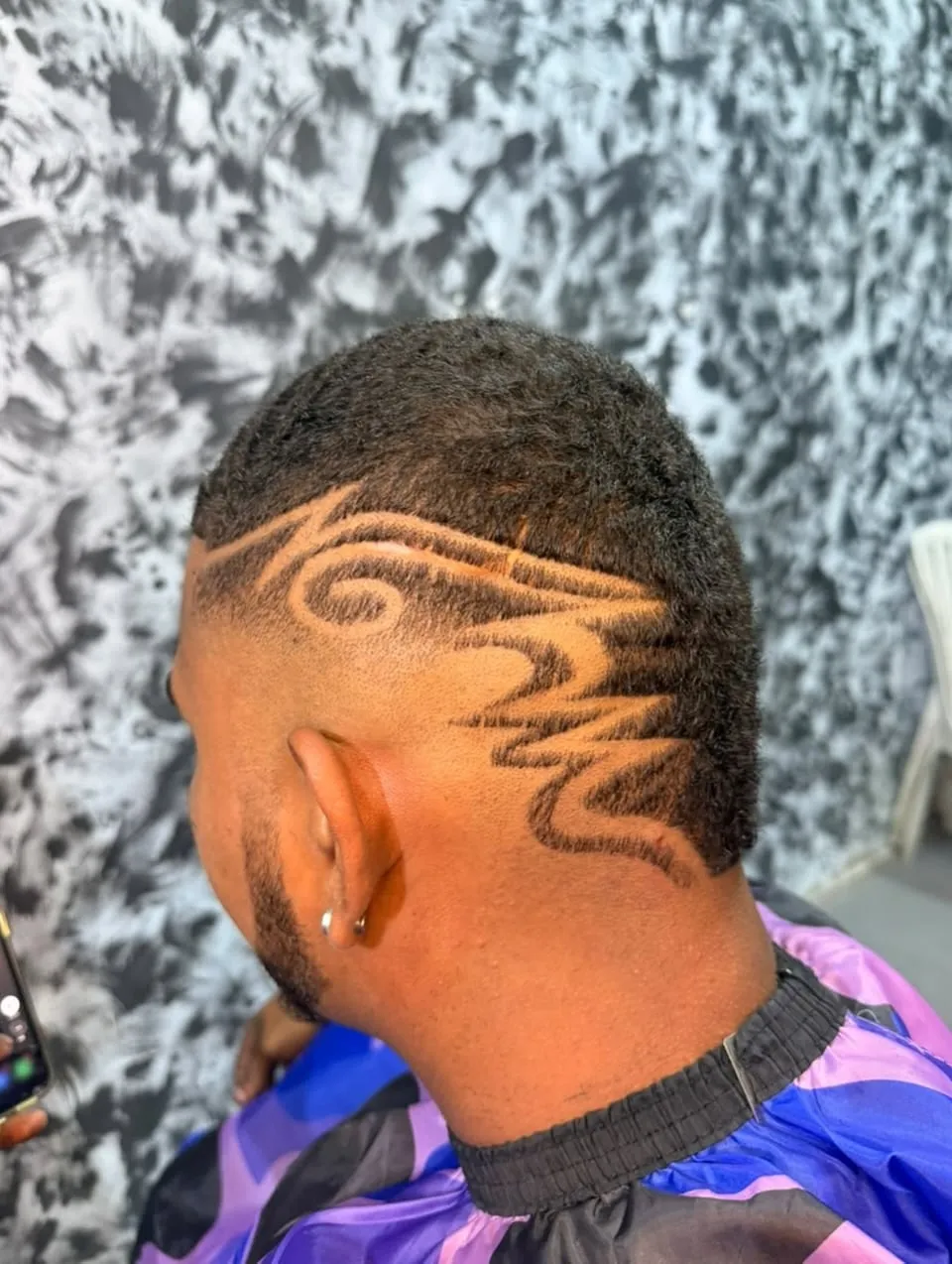 Desvanecido en cabello afro corto con un diseño tribal de espirales y picos en el costado de la cabeza