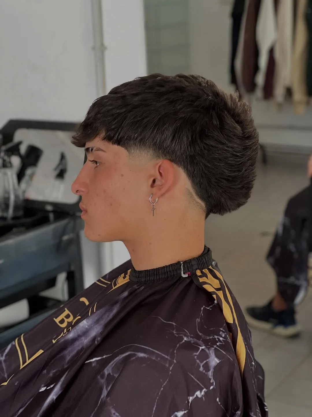 Taper fade de perfil con una sola línea diagonal detrás de la oreja y cabello castaño oscuro con fleco texturizado