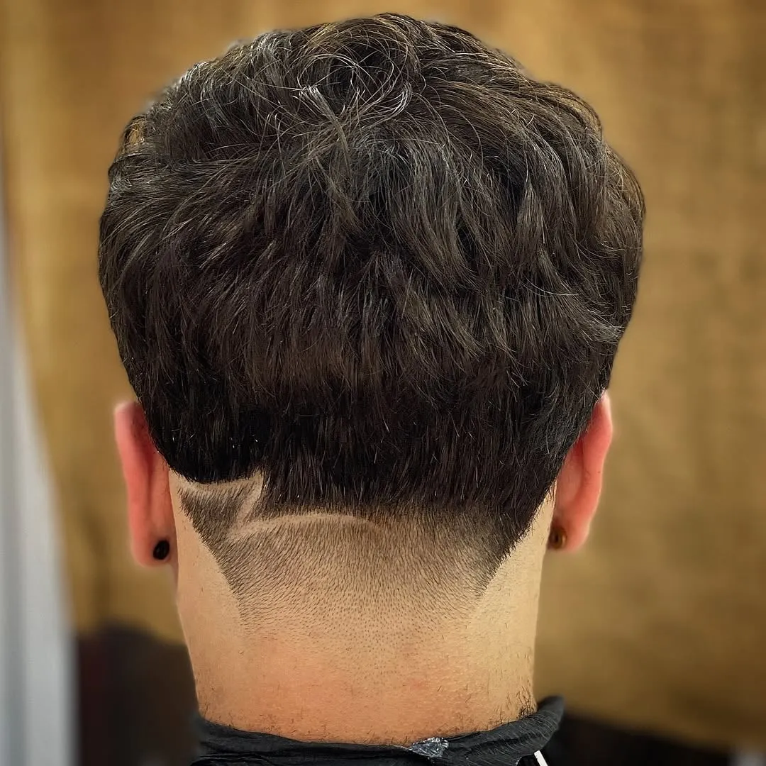 Taper fade visto de espaldas con la nuca en forma de V y una línea diagonal en el lado izquierdo en cabello castaño ondulado
