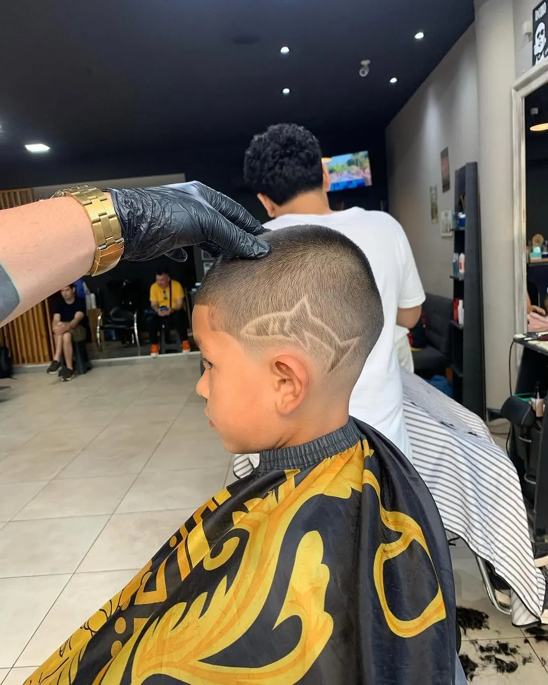 Niño en la barbería con desvanecido bajo y un diseño de tiburón dibujado en el costado de la cabeza
