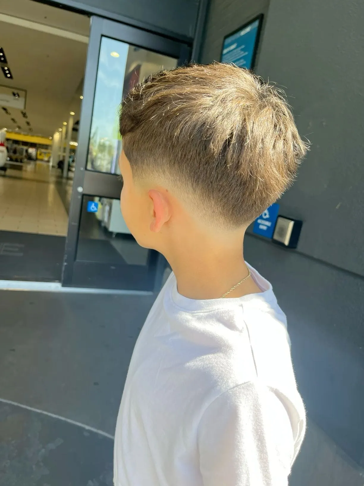 Taper fade en niño con cabello rubio texturizado visto de espaldas y de lado