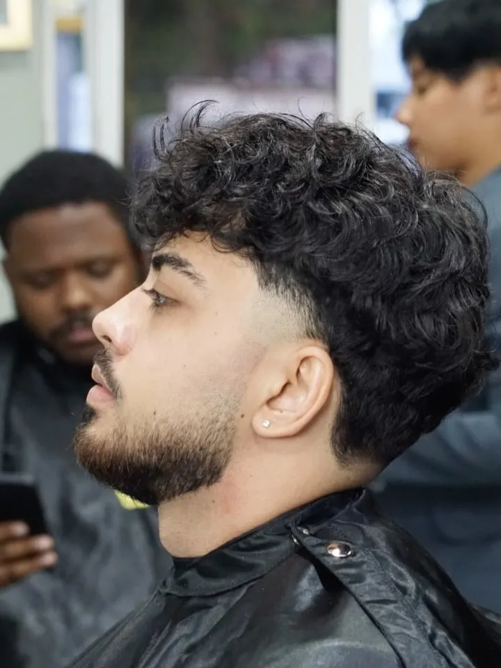 Taper fade en cabello rizado con volumen arriba y barba corta perfilada