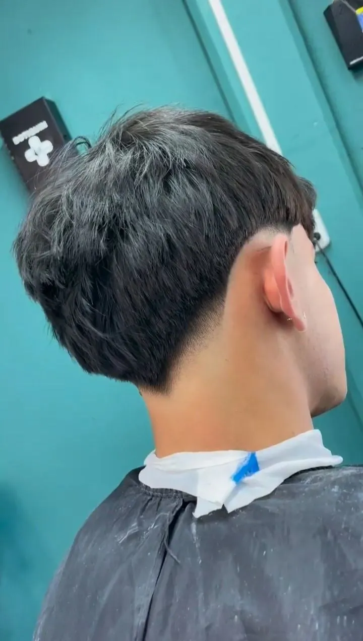 Taper fade con la nuca cortada en forma de V y cabello oscuro texturizado arriba