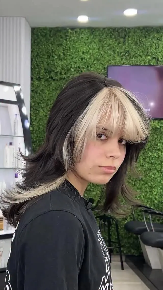 Mujer joven con wolf cut negro a media melena, mechas frontales rubias en el flequillo y capas desfiladas a los lados