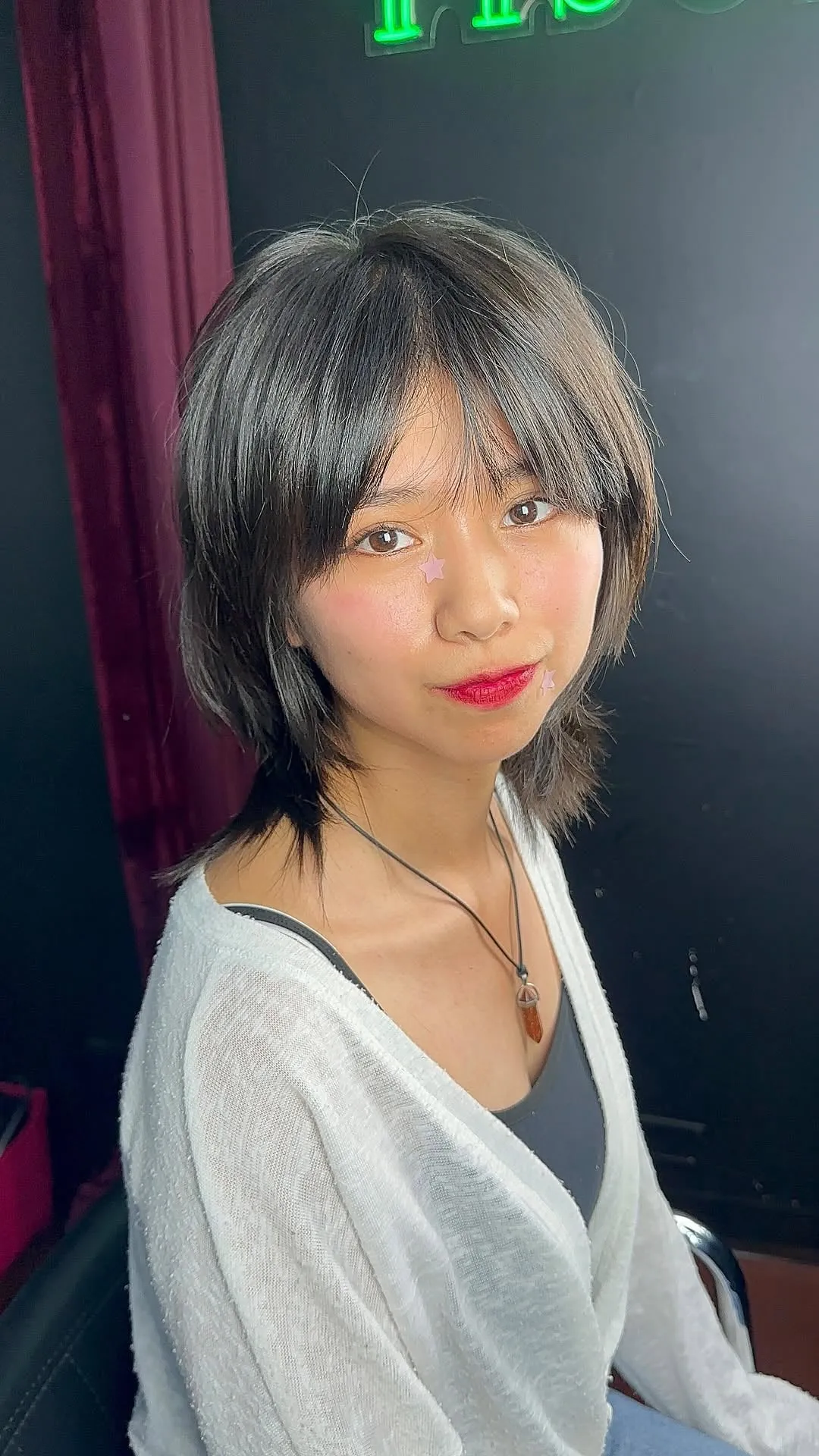 Mujer joven con wolf cut corto estilo coreano en cabello negro lacio, flequillo cortina y capas finas sobre el cuello