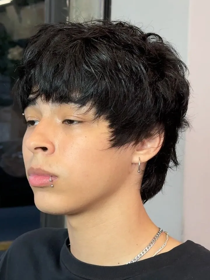Joven de perfil con wolf cut corto en cabello negro, fleco desfilado sobre los ojos y nuca algo más larga