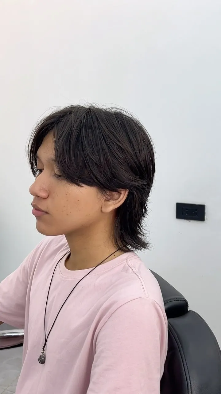 Joven de perfil con wolf cut en cabello negro lacio, flequillo largo hacia adelante y nuca desfilada que tapa el cuello