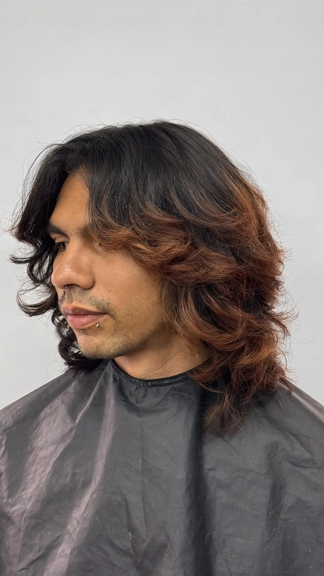 Hombre de perfil con wolf cut largo en cabello ondulado oscuro con reflejos cobrizos, capas hasta el hombro