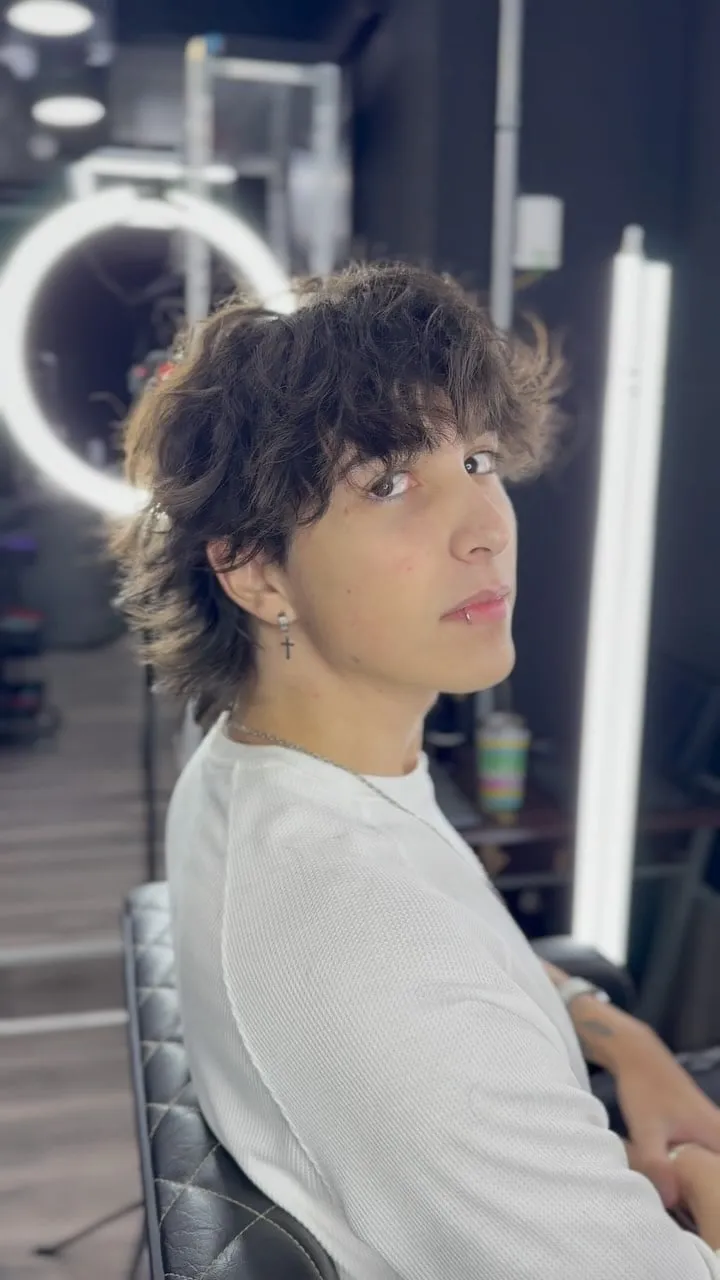 Joven con wolf cut en cabello rizado castaño oscuro, rizos con volumen arriba, flequillo rizado y nuca larga