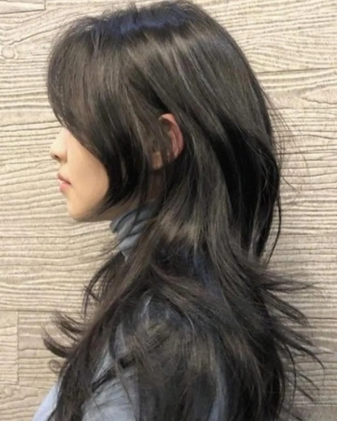 Mujer de perfil con wolf cut largo en cabello negro lacio, capas cortas en la coronilla y mechones desfilados hasta media espalda