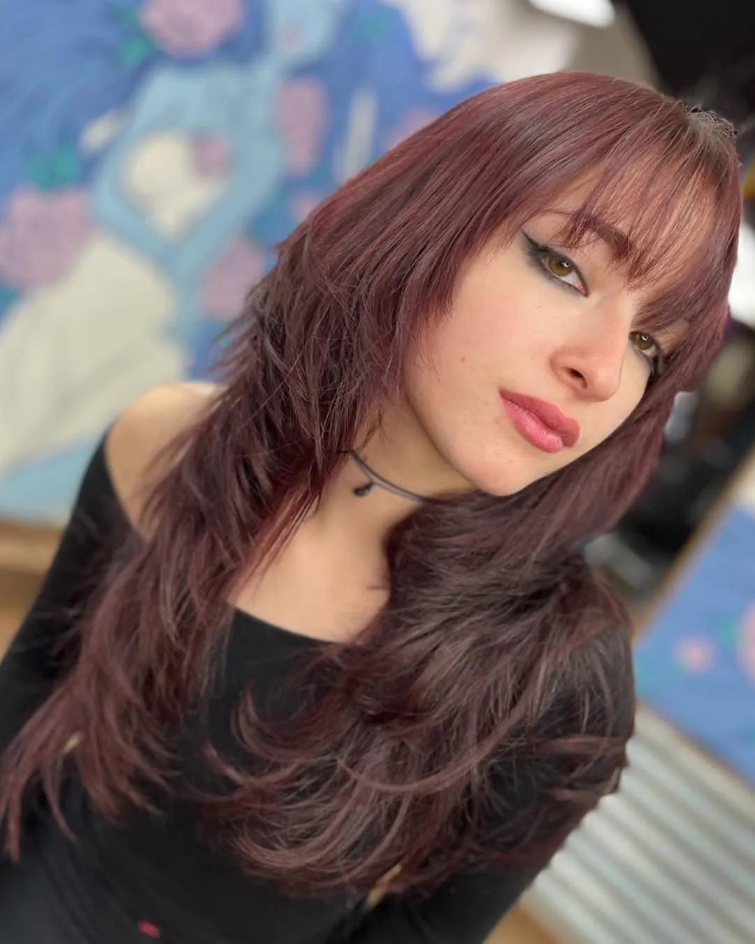 Mujer joven con wolf cut largo en tono rojizo, flequillo recto a las cejas y capas desfiladas que caen sobre los hombros