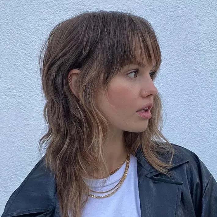 Mujer de perfil con wolf cut castaño a media melena, flequillo largo desfilado y mechas claras en las puntas