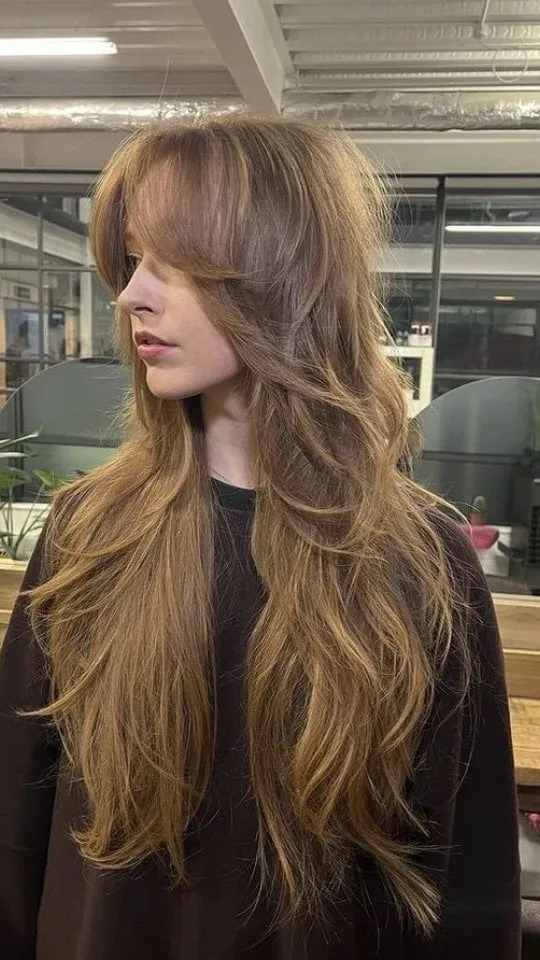 Mujer de perfil con wolf cut muy largo castaño claro, capas desfiladas desde la coronilla hasta la cintura y flequillo largo de lado