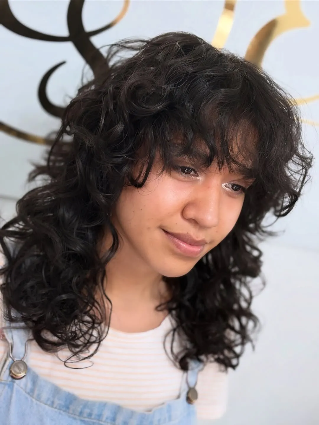 Mujer joven con wolf cut en cabello negro ondulado, flequillo desfilado y capas con volumen a la altura del pecho