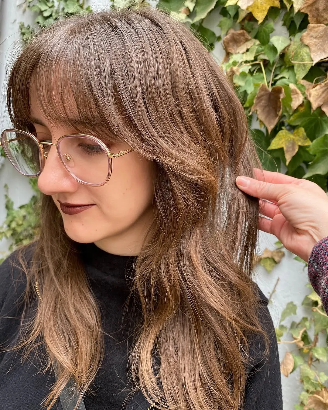 Mujer con lentes y wolf cut en pelo liso castaño con mechas, flequillo cortina largo y capas desfiladas a la altura del pecho
