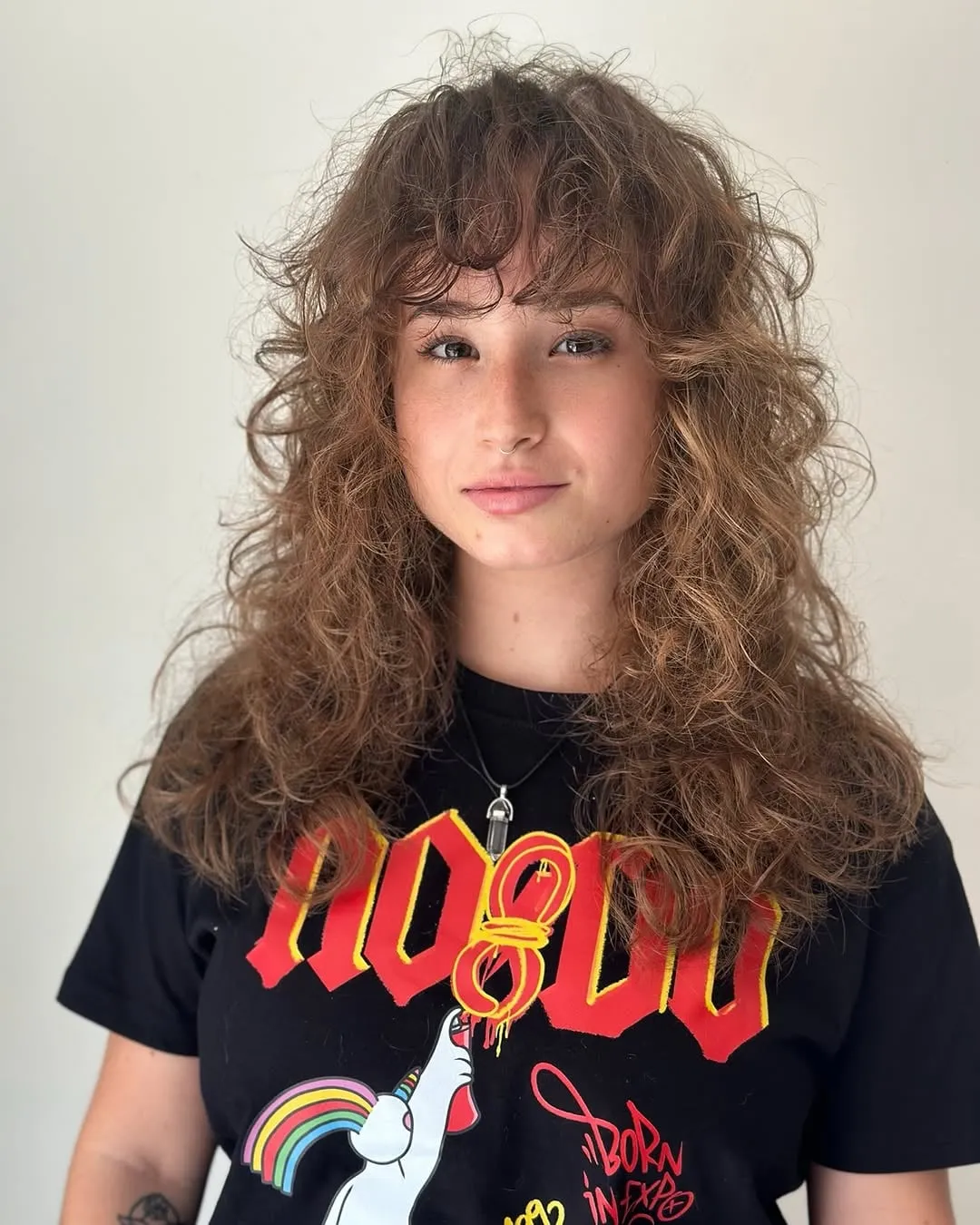 Mujer con wolf cut en cabello rizado castaño largo, volumen en la coronilla y flequillo rizado sobre la frente